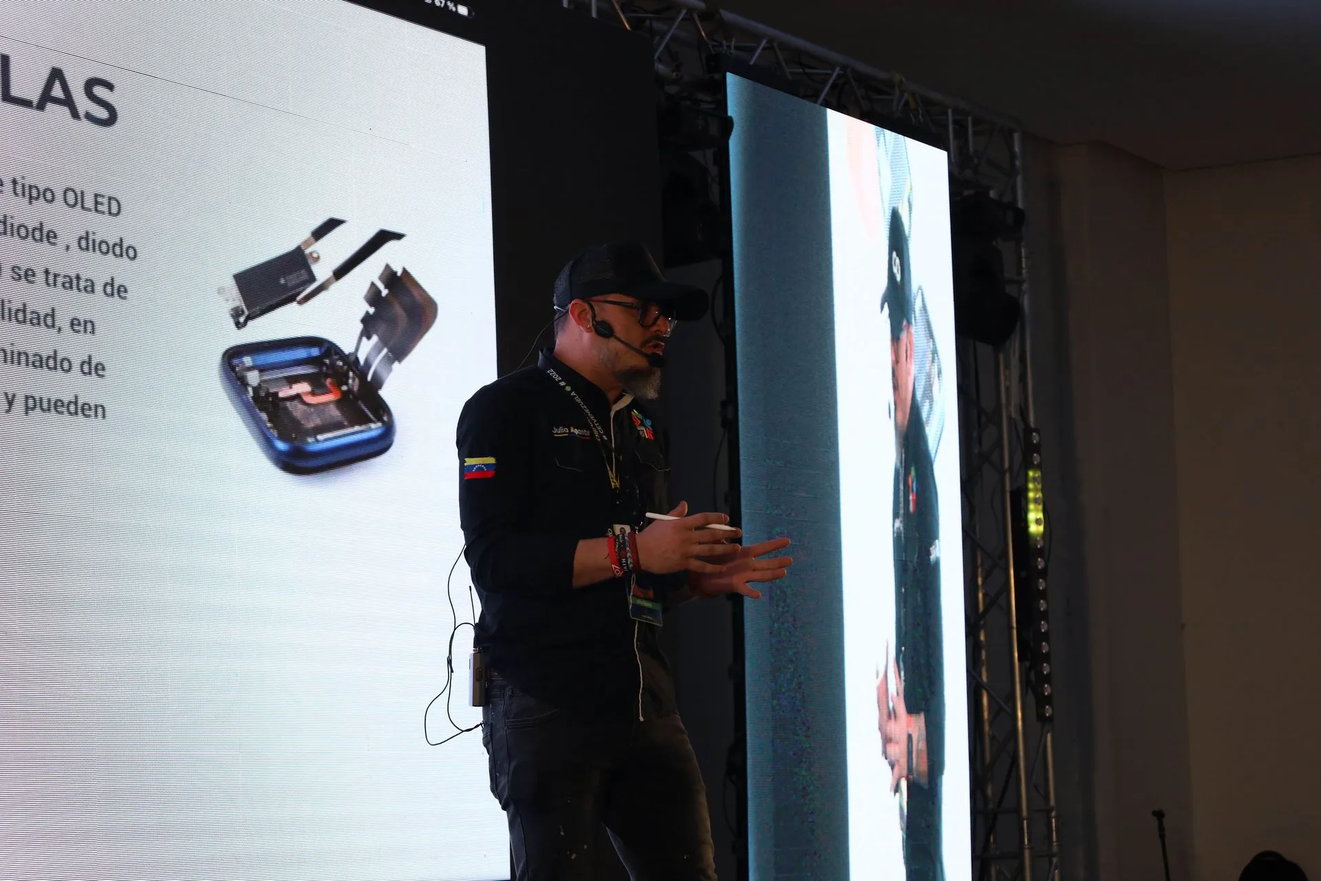 Julio Aponte durante una ponencia, con una diapositiva de reparación de pantallas OLED al fondo.